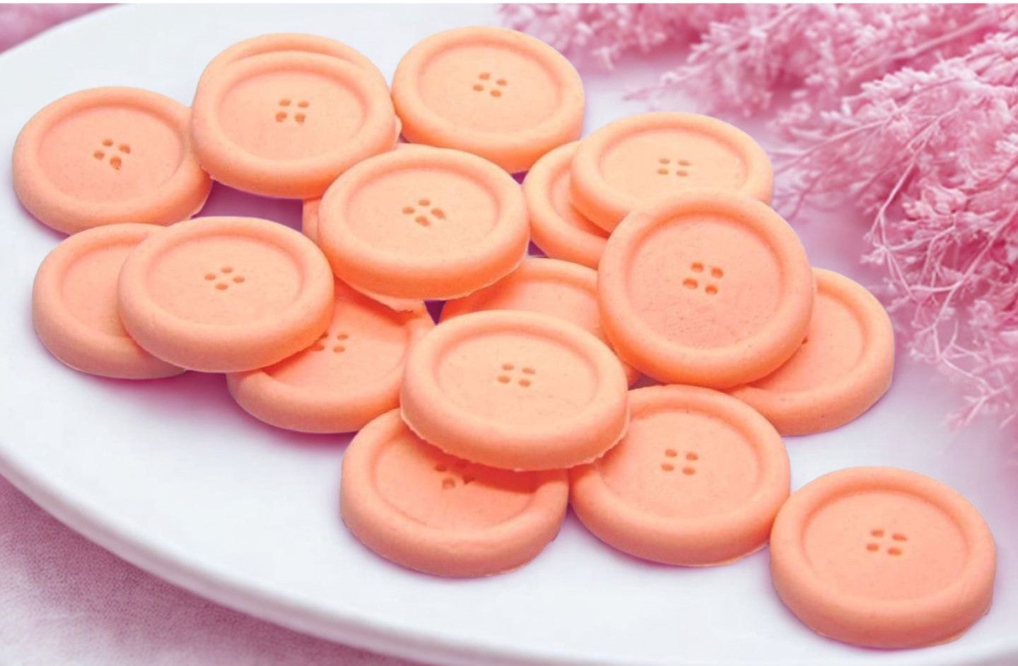 Peach coloured edible buttons for baked goods decorations shown in a white dish with a pink cloth in the background