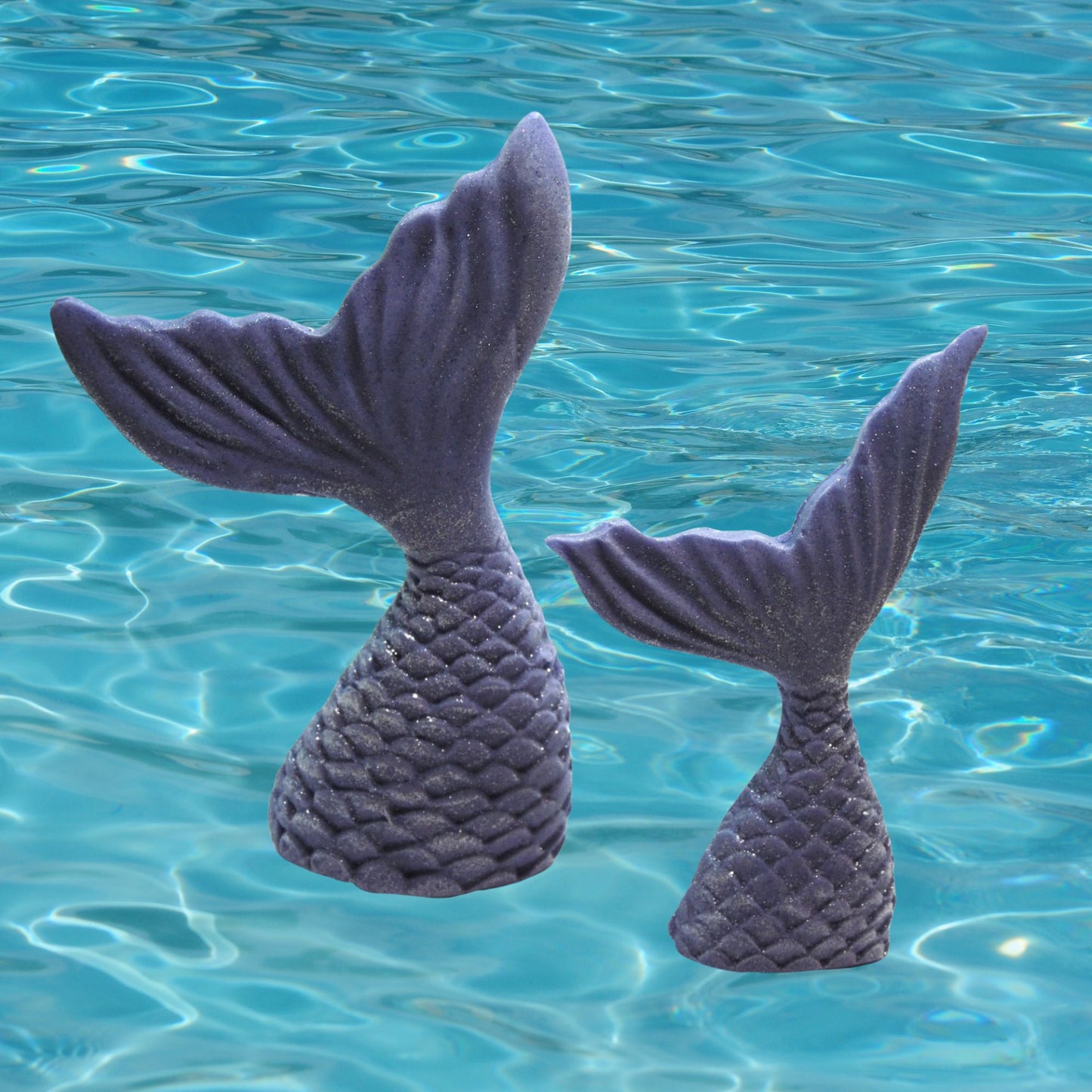 Two purple mermaid tails cake toppers floating on a blue water surface