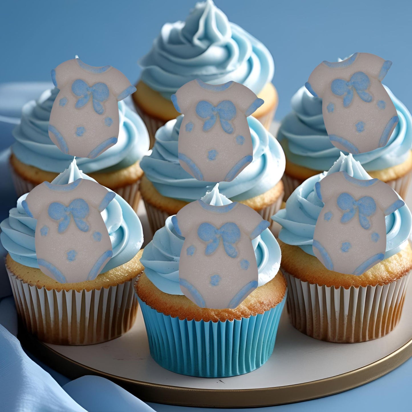 Cupcakes with blue frosting and edible blue baby onesie decorations on a plate.