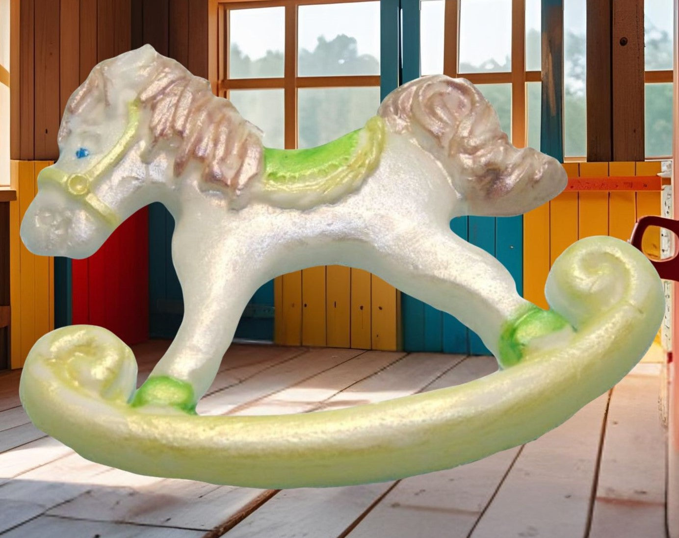 White and green rocking horse cake topper decorations shown with an background image in a playroom with wooden floor and colorful walls.