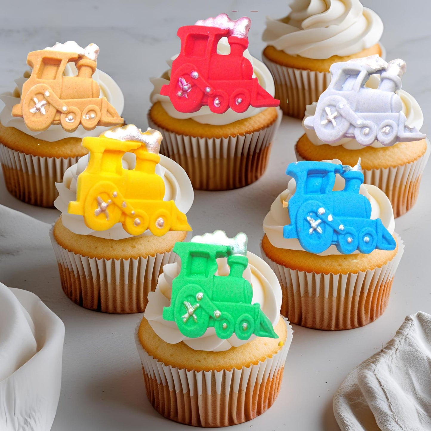 Cupcakes with train-themed decorations on a white surface