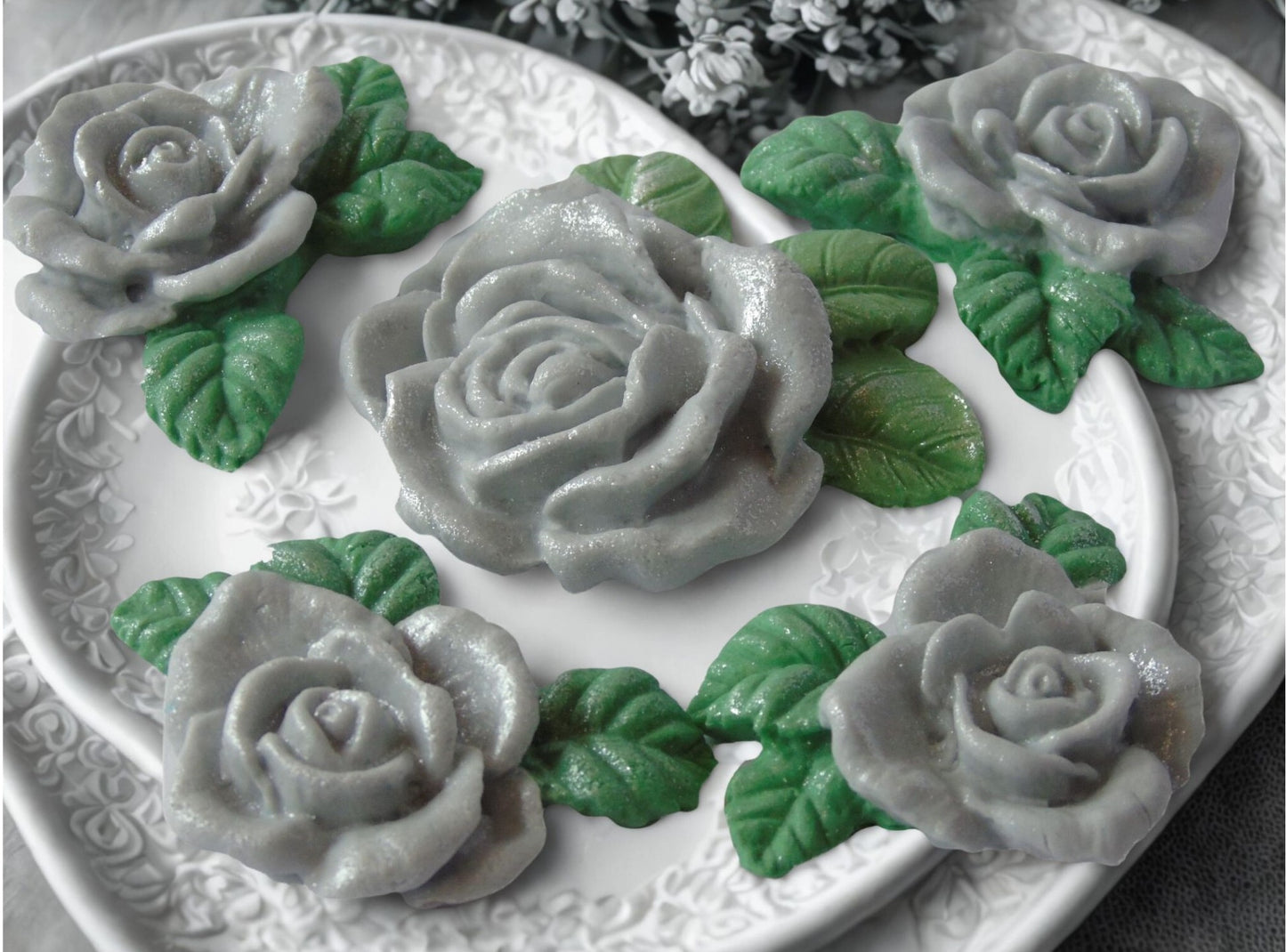 A set of edible glittered Silver rose garland cake toppers with a large centre rose, on a plate