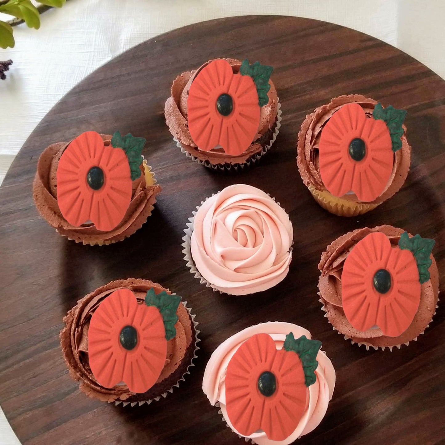 Cupcakes decorated with edible poppies on a wooden surface